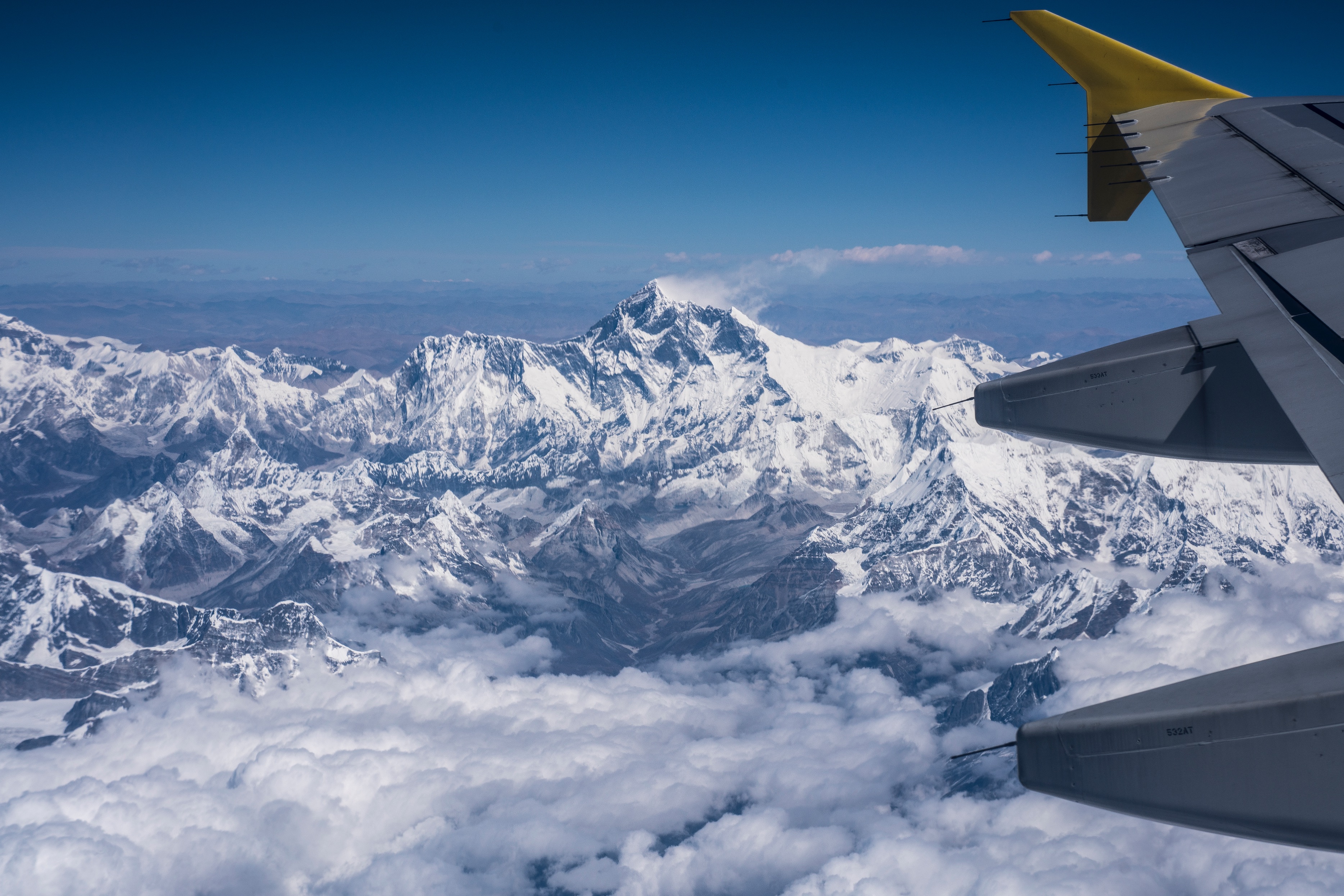 View from plane window over snowy mountain tops including wing of plane